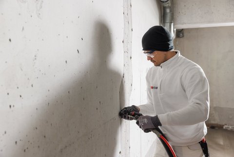 ISOTEC Mitarbeiter bohrt Löcher in Betonwand.